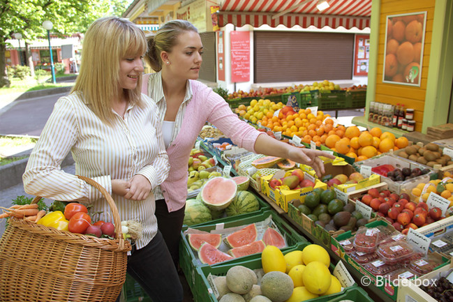 Zwei junge Frauen kaufen auf einem Obst- und Gemüsemarkt ein.