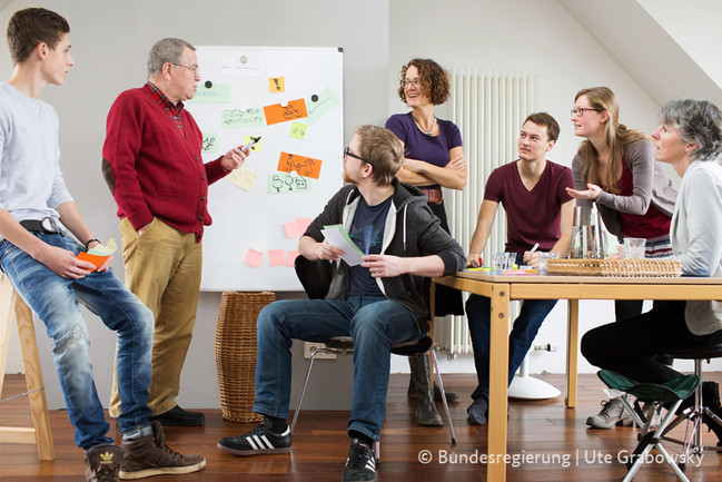 Personen unterschiedlichen Alters diskutieren vor einem Flipchart.