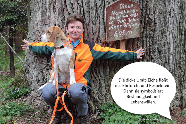 Försterin Manuela Seeber mit Hund Mika vor einer Eiche.