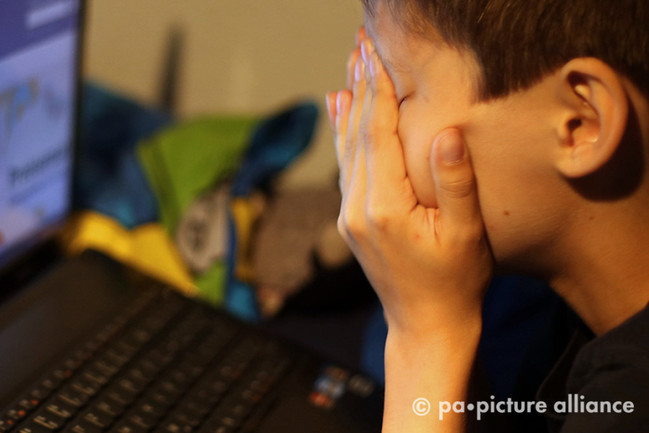  Ein Junge reibt sich vor seinem Laptop  die Augen.