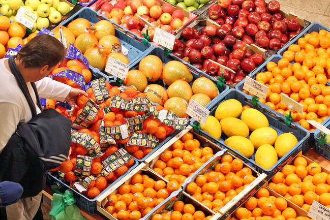 Ein Mann steht an einem Obststand mit Orangen, Äpfeln und Pomelo. 